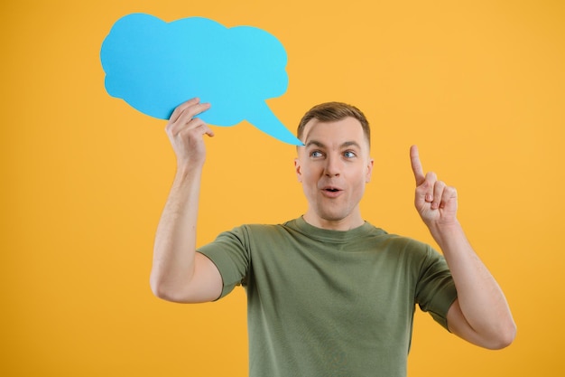 Cheerful young male pointing up and holding empty speech bubble with blank space for quote against vivid yellow background