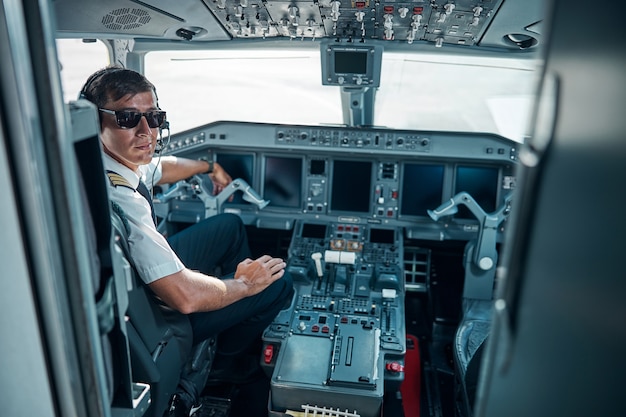 Foto un giovane allegro in uniforme da aereo e occhiali vicino al controllo si sta preparando per il jet in volo