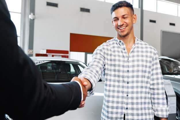 Cheerful young man customer buys a new car in a dealership