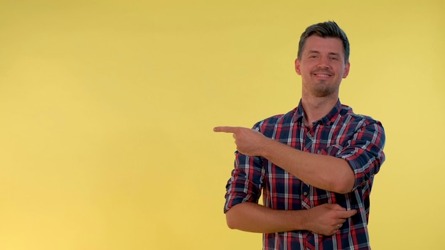 Photo cheerful young man getting a tip from somebody and showing forefinger to the side yellow background