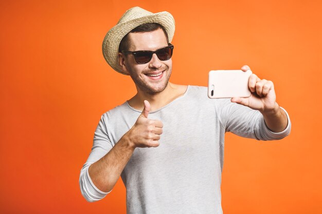 Cheerful young man in hat and sunglasses taking selfie with smartphone
