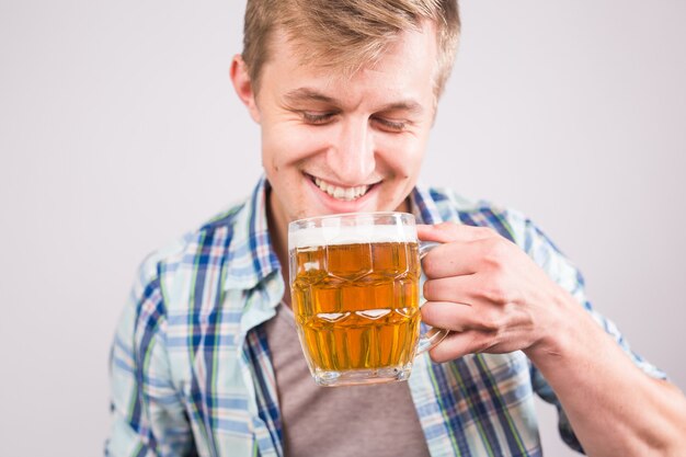 Cheerful young man holding a beer mug full of beer and smiling on white background.