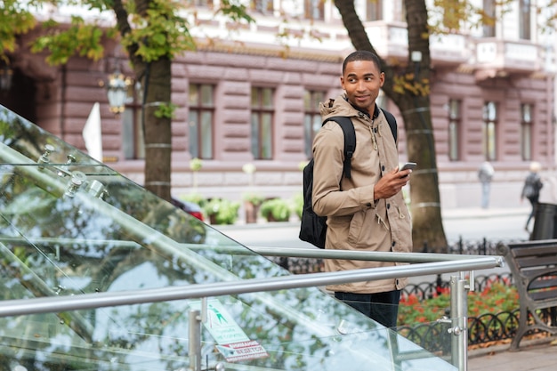 Cheerful young man holding his phone in hands and looking aside