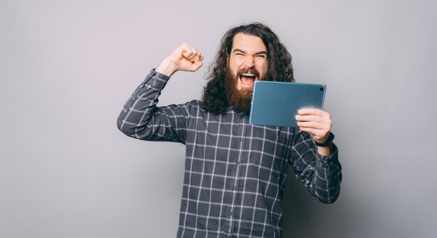 A cheerful young man is excited because he won a game on a tablet