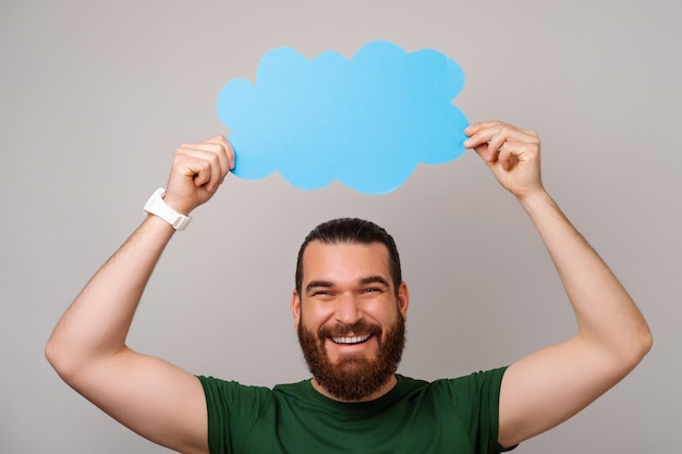 Cheerful young man is holding a blue cloud shaped bubble speech above his head