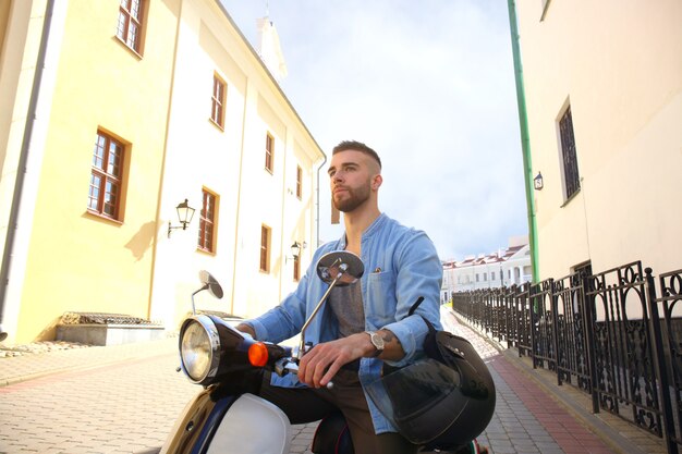 Cheerful young man is riding on scooter in town.