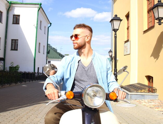 Cheerful young man is riding on scooter in town.