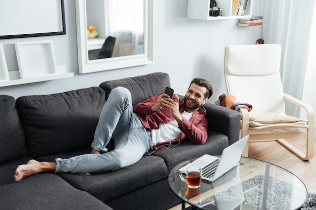 Cheerful young man lies on sofa chatting by phone.