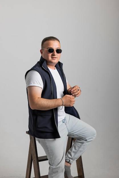 A cheerful young man model in a sleeveless regular solid jacket and a black sunglass posing in multi