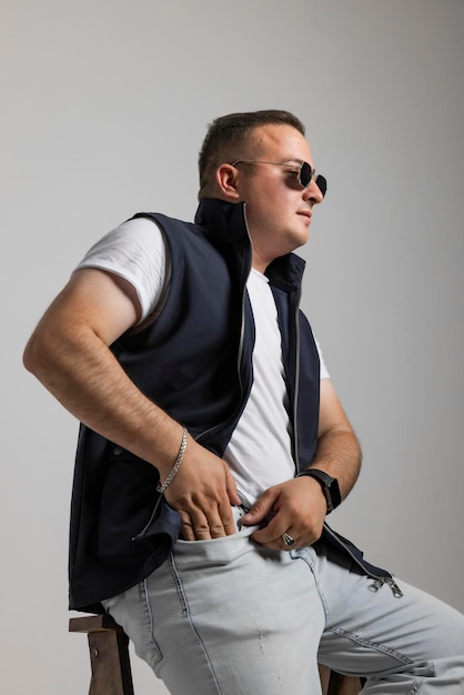 Photo a cheerful young man model in a sleeveless regular solid jacket and a black sunglass posing in multi