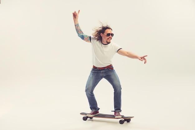 Фото Веселый молодой человек на скейтборде изолирован на белом фоне студии в стиле ретро