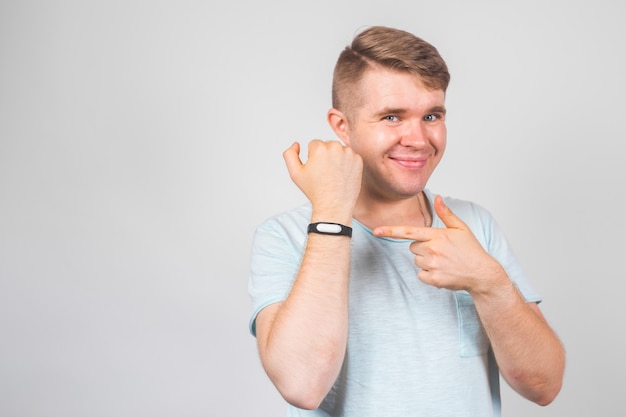 Cheerful young man standing and pointing on fitness tracker over grey