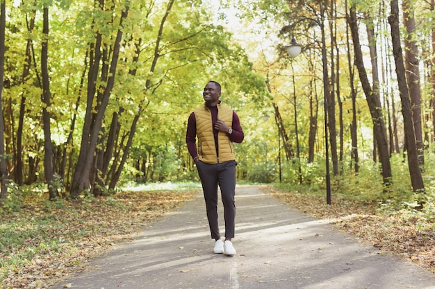 Il giovane allegro in vestiti alla moda cammina nel parco di autunno il concetto di giornata calda e soleggiata di autunno di