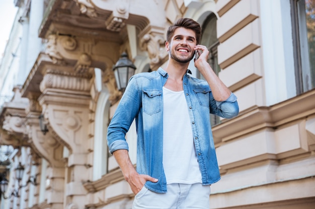 Cheerful young man walking and talking on cell phone in the city