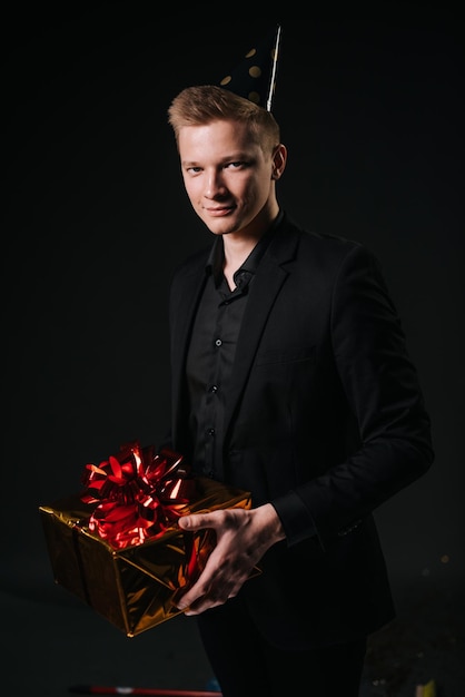 Cheerful young man with in a festive cap holds a holiday box with a gift