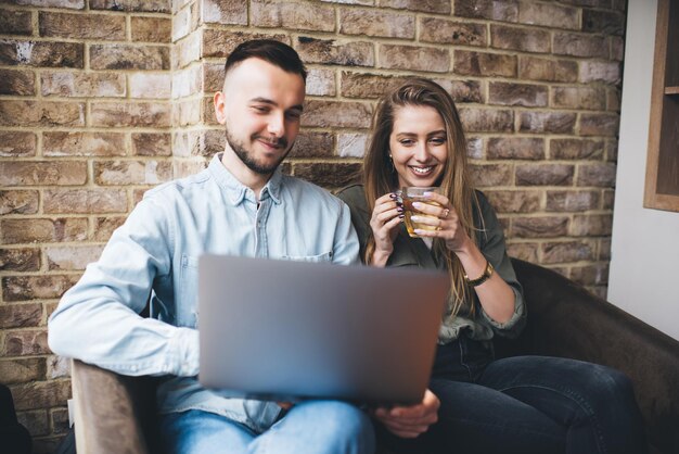 Photo cheerful young modern couple browsing laptop having drinks in cafe