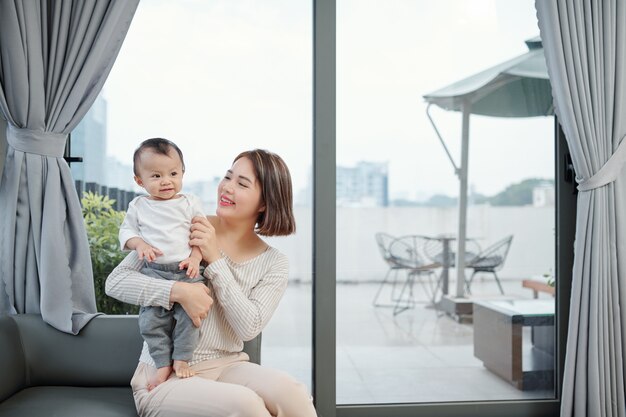 Cheerful young mother playing with adorable little baby at home