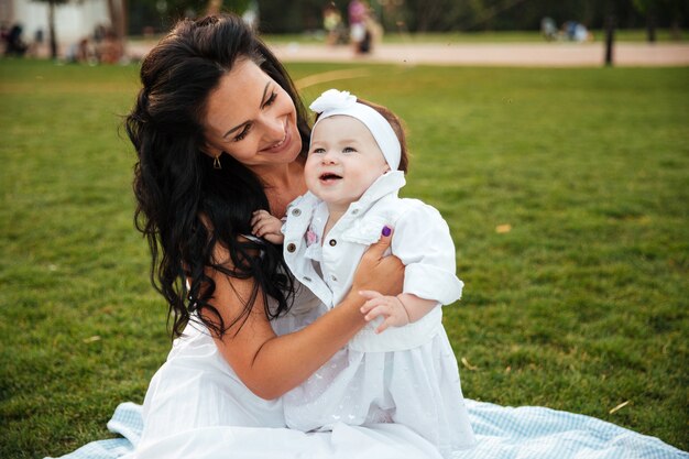 Cheerful young mother sitting with her little daughter outdoors