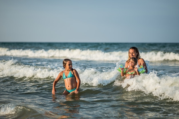 Cheerful young mother swims in the sea with her charming little daughters and enjoy the long-awaited weekend on a sunny summer day