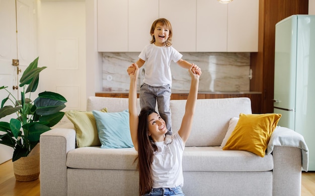 Cheerful young mother with little toddler daughter having fun at home together
