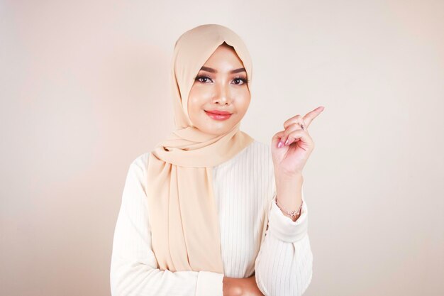 Cheerful young Muslim Asian woman pointing side to copy space with smile