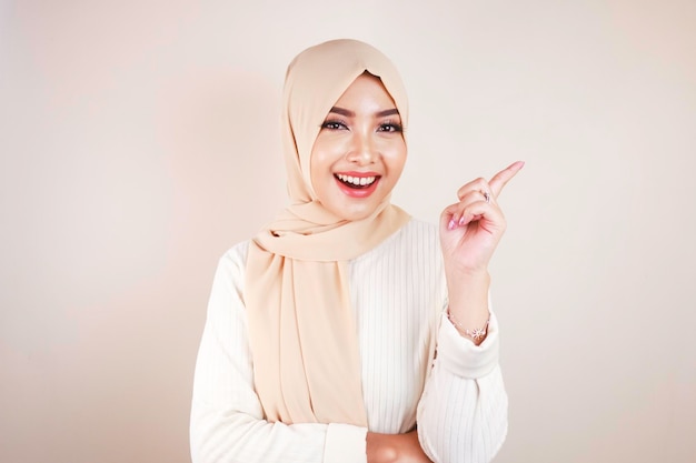 Cheerful young Muslim Asian woman pointing side to copy space with smile