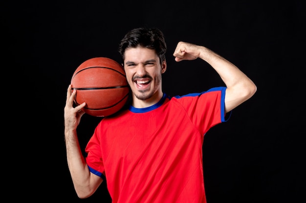 Cheerful young player with basketball on black