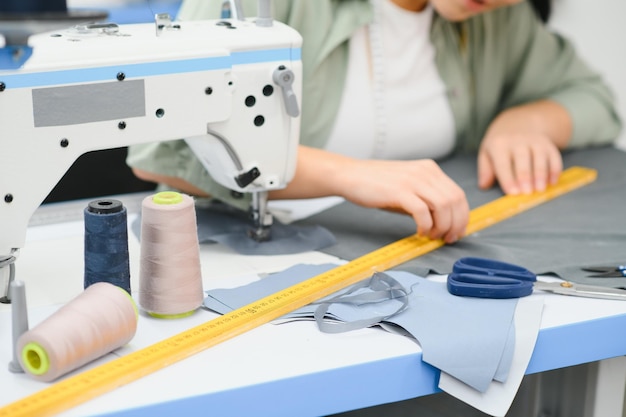 Cheerful young seamstress sits at the table with working things in atelier