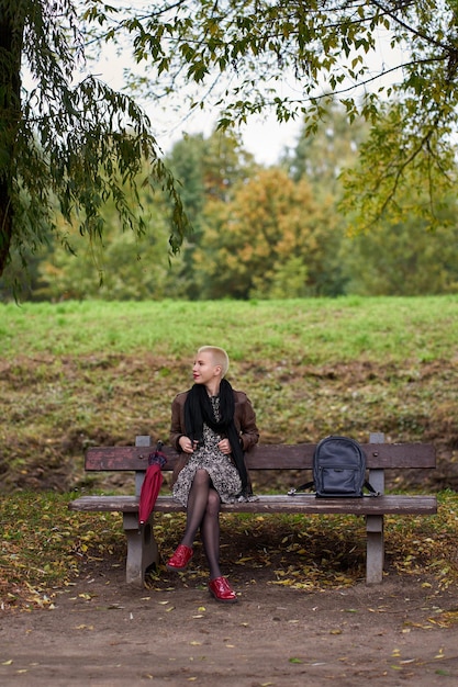 写真 ベンチに座って、秋の公園でリラックスした陽気な若い短い髪のブロンドの女性