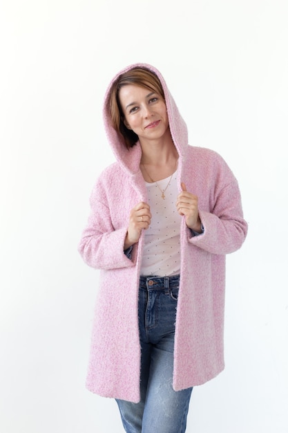 Photo cheerful young slim woman posing in pink coat with hood over white background.