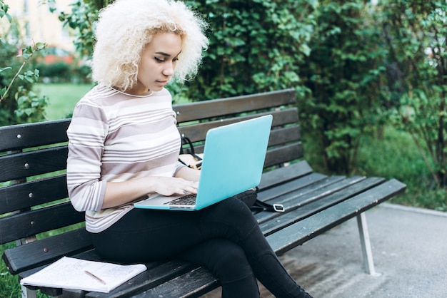 Cheerful young student girl outdoors is sitting on the bench