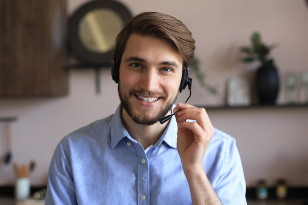 Cheerful young support phone male operator in headset, at workplace while using laptop, help service and client consulting call center concept.