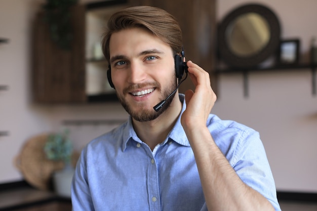 ラップトップを使用しながら職場で、ヘッドセット、ヘルプサービス、クライアントコンサルティングコールセンターのコンセプトで陽気な若いサポート電話男性オペレーター。