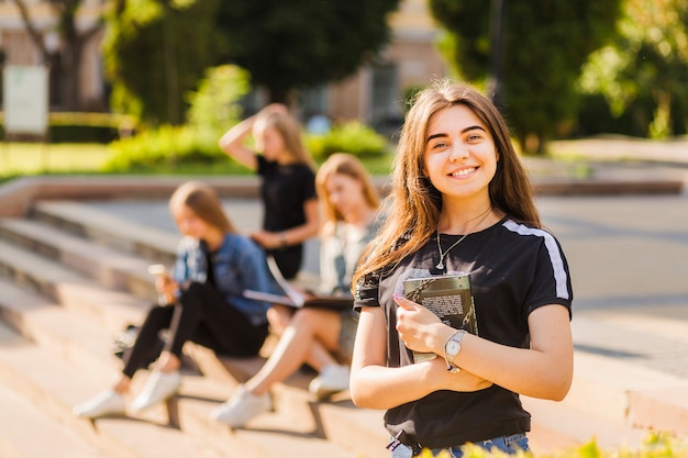 Photo cheerful young teen girl with book near friends