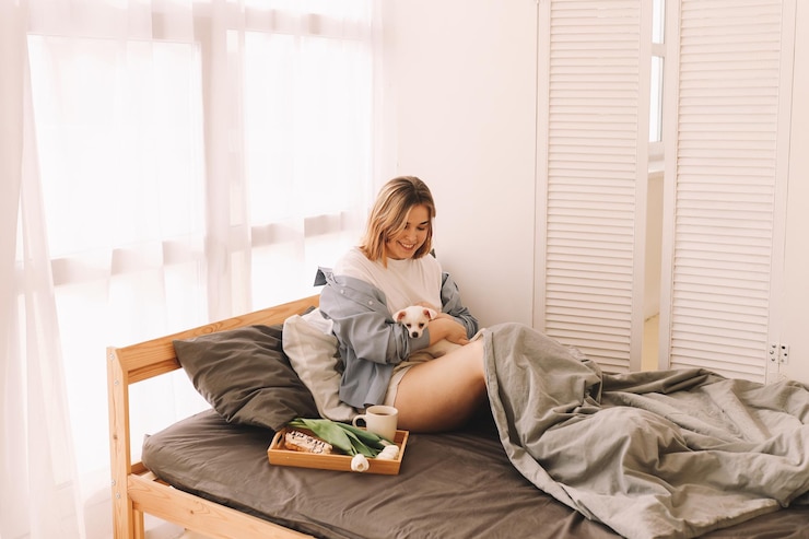 Photo a cheerful young teenage woman plays with her pet a small dog in bed in the morning in a cozy house