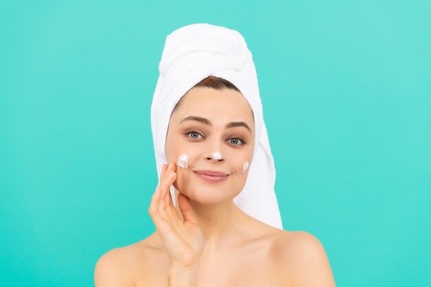 Cheerful young woman apply face cream on blue background