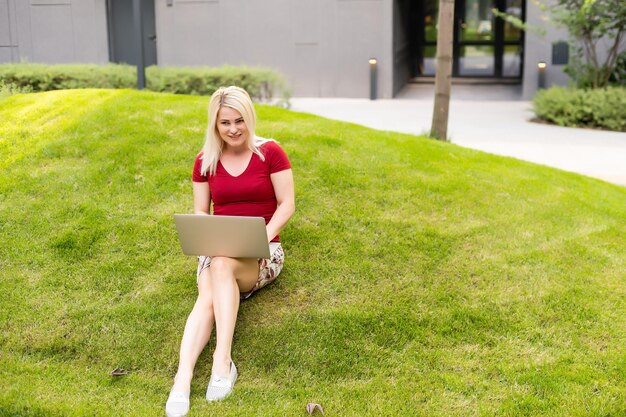 Cheerful young woman browsing internet on her laptop outdoors at the park