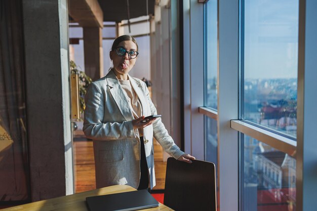 Cheerful young woman in casual wear having telephone conversation sitting at working place near laptop in office smiling female freelancer calling to colleague for share good news about business