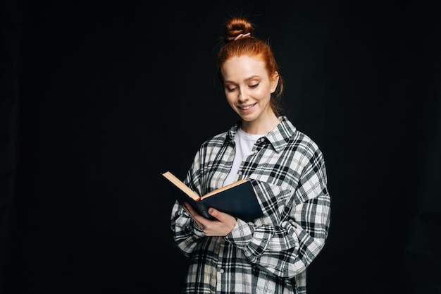 黒の孤立した背景の本を読んで陽気な若い女性の大学生