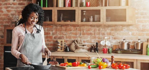 cheerful young woman cooking healthy food at kitchen