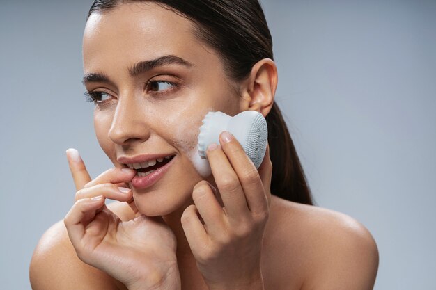 Cheerful young woman doing face cleaning with cosmetics device