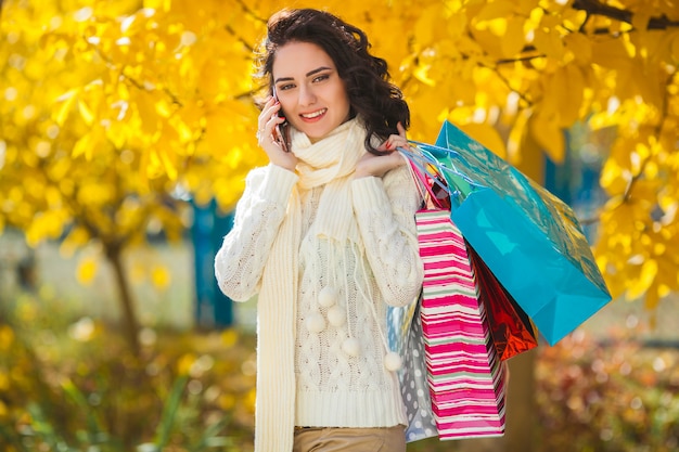 陽気な若い女性が買い物をしています。ショッピングバッグと秋の屋外の美しい少女。