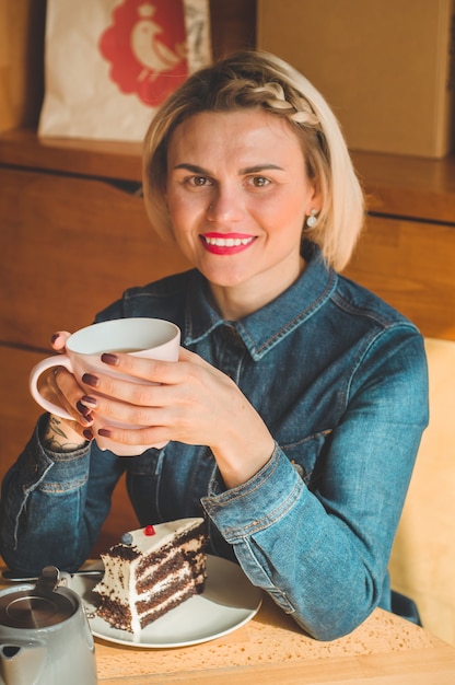 温かいコーヒーやお茶を飲みながらカフェに座っている陽気な若い女性。一杯のコーヒーを保持している魅力的な女性。