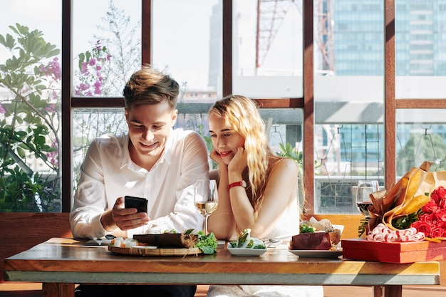 カフェで夕食を楽しんだり、スマートフォンで面白い動画を見ている陽気な若い女性