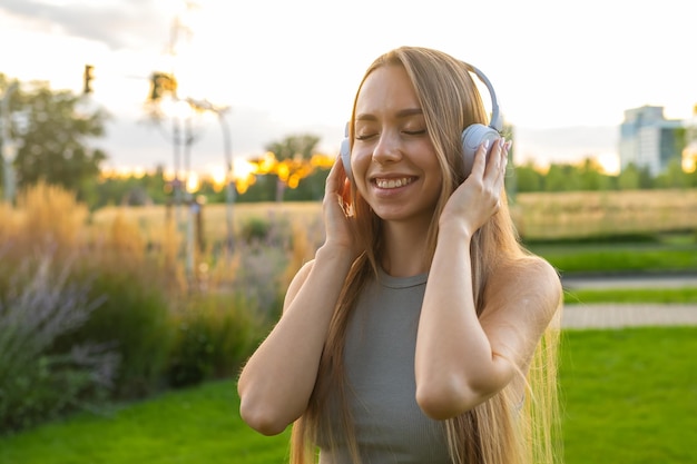 Веселая молодая женщина любит слушать музыку и петь, сидя в парке счастливая женщина в
