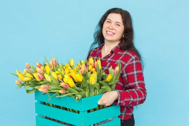 青い背景の上のチューリップの箱と陽気な若い女性の花屋