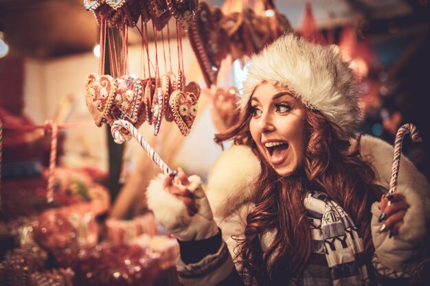 Веселая молодая женщина развлекается на рождественской ярмарке на городской улице в новогоднюю ночь.