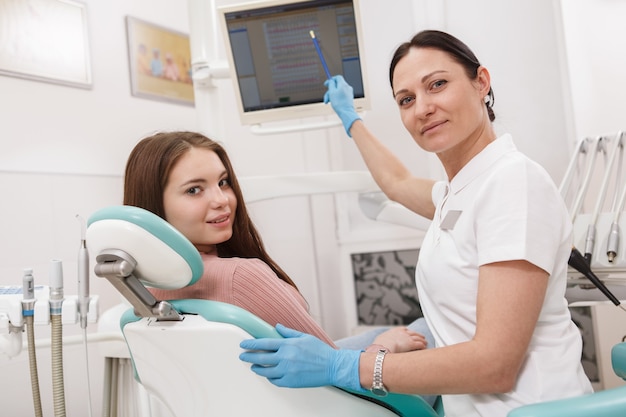 Cheerful young woman and her dentist smiling to the camera during their dental appointment