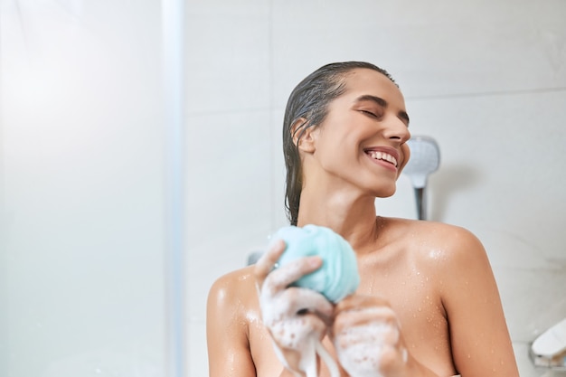 Cheerful young woman holding exfoliating loofah sponge