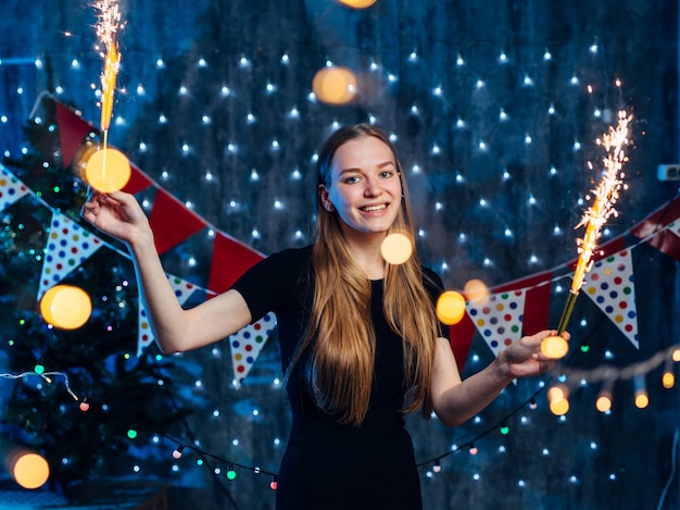 Cheerful young woman holding sparkler in hand.